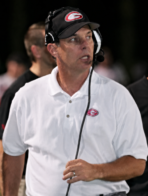 Joe Kersting coaching on the sideline wearing a headset and a team cap.